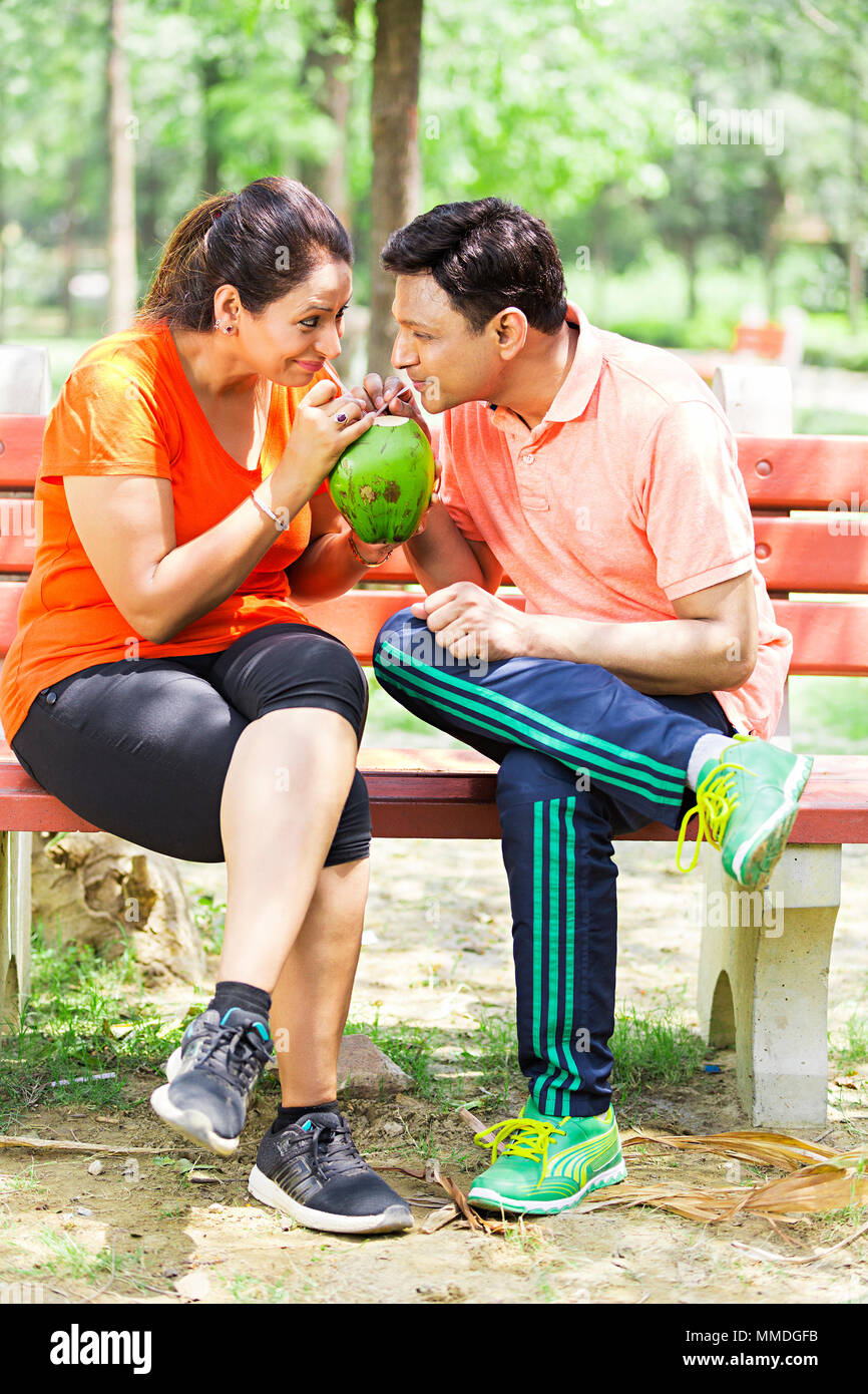 Romantische Ehepaar sitzen Bank Sipping Kokosmilch erfrischenden Garten Stockfoto