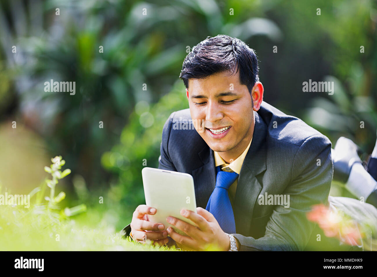 Ein Unternehmer Mitarbeiter Gras liegend Lesen Text-Messaging Mobile Tablet-Pc Garten Stockfoto