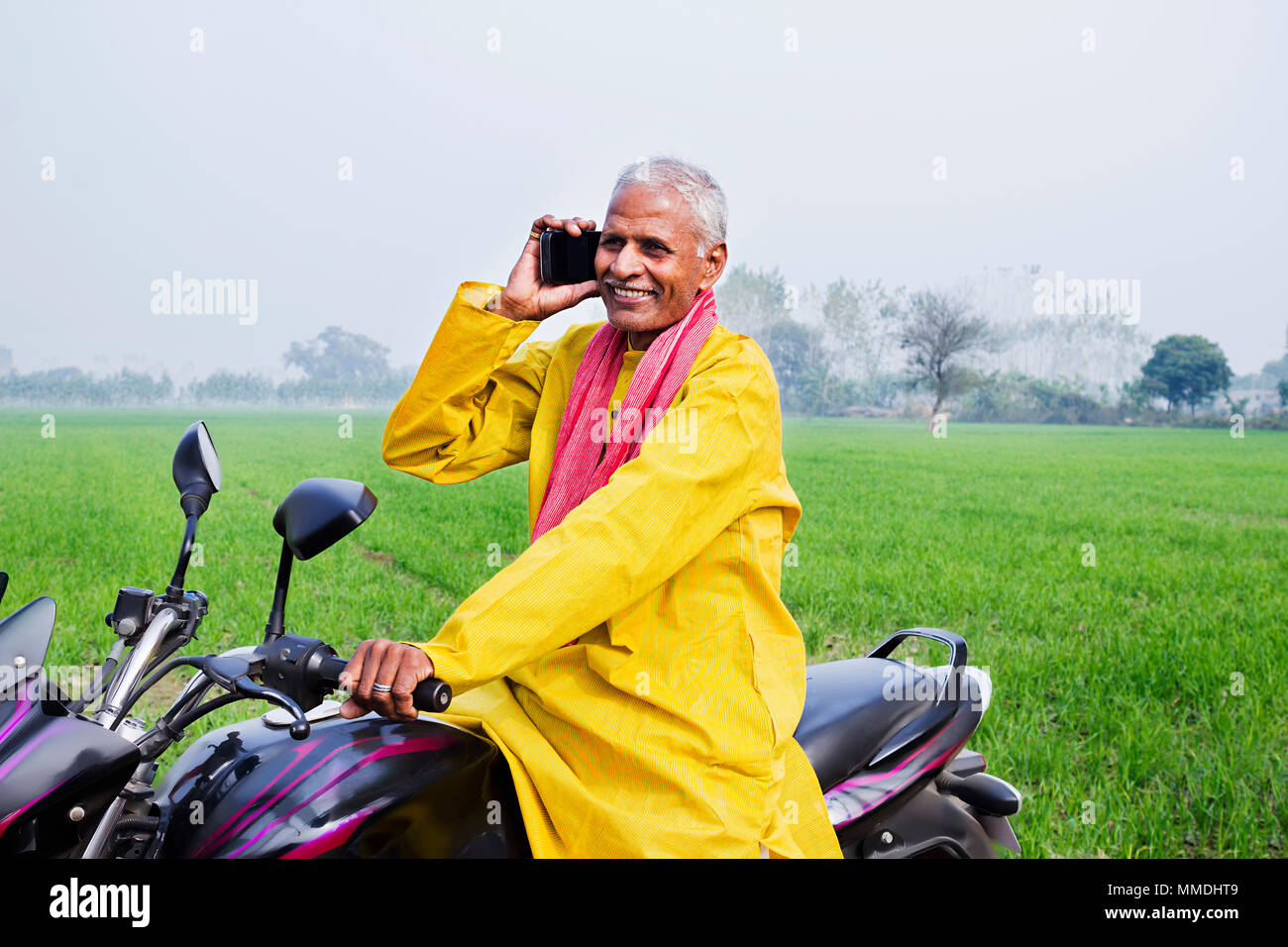 Eine ländliche Dorfbewohner alter Mann reiten Motorrad und Reden Handy Feld Stockfoto
