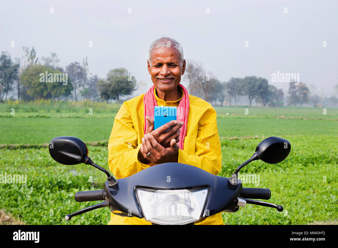 Alter Mann Dorfbewohner sitzen Roller, lesen SMS SMS-Smartphone Bauernhof Dorf Stockfoto