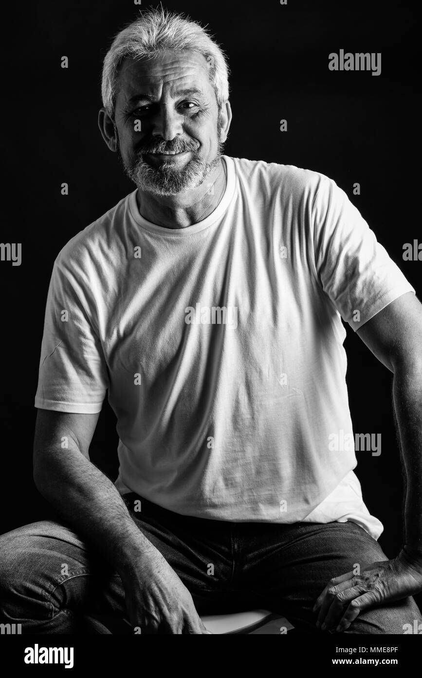 Reifer Mann lächelnd in die Kamera schauen. Älterer Mann mit weissem Haar und Bart lachend legere Kleidung auf schwarzem Hintergrund isoliert. Studio shot Stockfoto