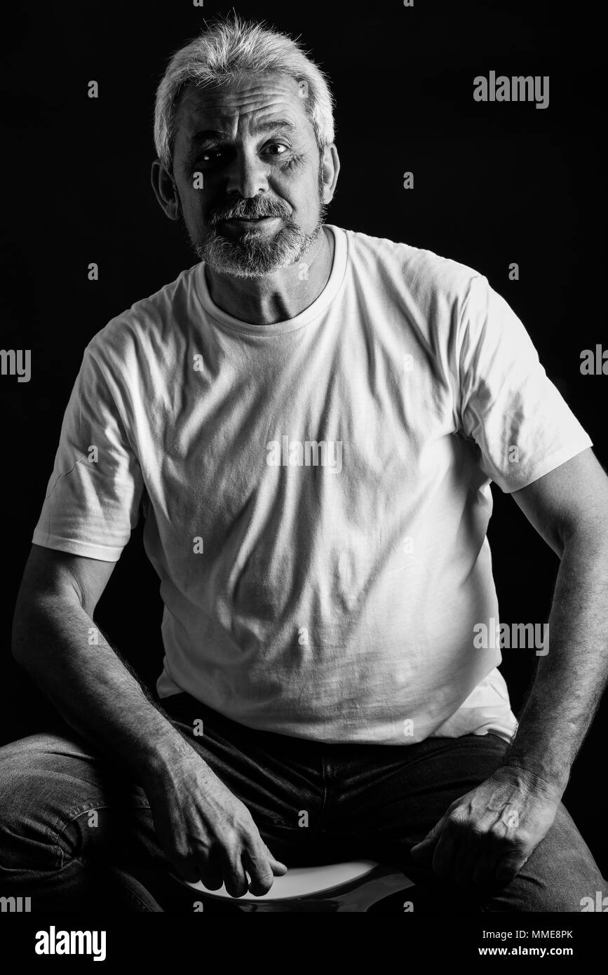 Reifer Mann lächelnd in die Kamera schauen. Älterer Mann mit weissem Haar und Bart lachend legere Kleidung auf schwarzem Hintergrund isoliert. Studio shot Stockfoto