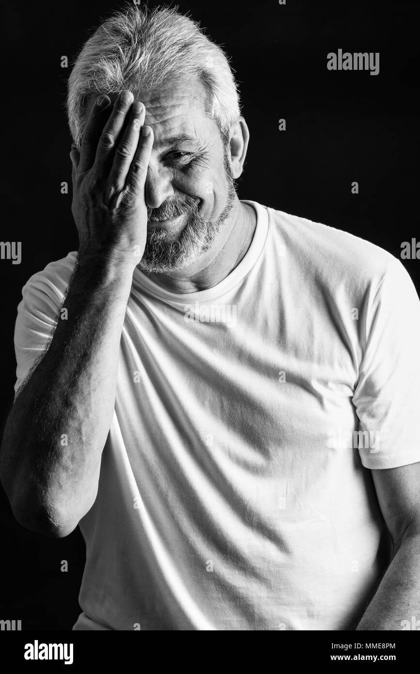 Porträt eines reifen Menschen ein Lächeln auf die Kamera schaut. Älterer Mann mit weissem Haar und Bart lachend legere Kleidung auf schwarzem Hintergrund Stockfoto