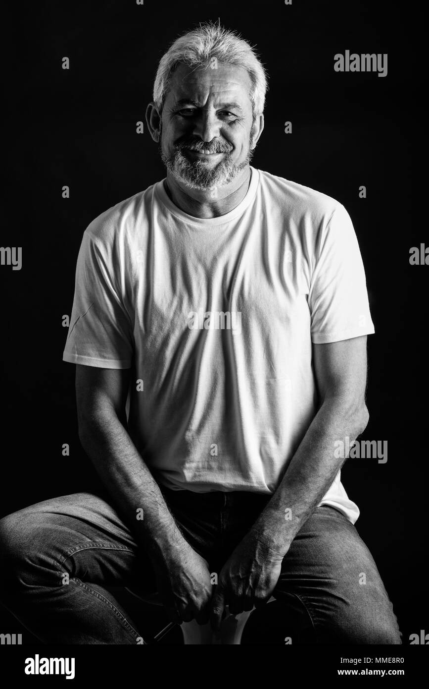 Reifer Mann lächelnd in die Kamera schauen. Älterer Mann mit weissem Haar und Bart lachend legere Kleidung auf schwarzem Hintergrund isoliert. Studio shot Stockfoto