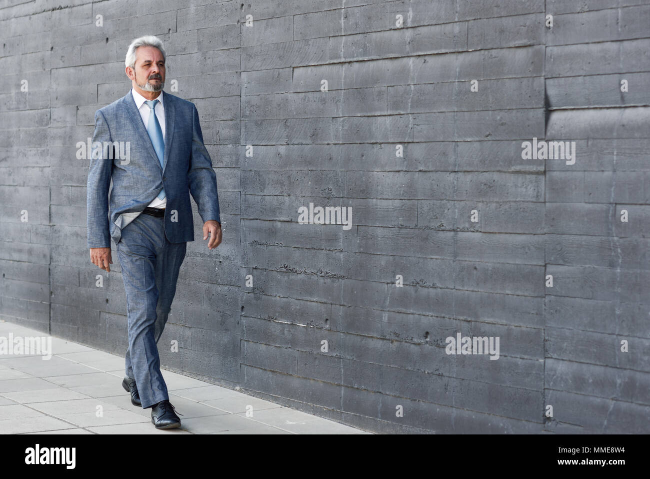 Senior Geschäftsmann zu Fuß außerhalb der modernen Bürogebäude. Erfolgreiche Mann mit Anzug und Krawatte im städtischen Hintergrund. Stockfoto