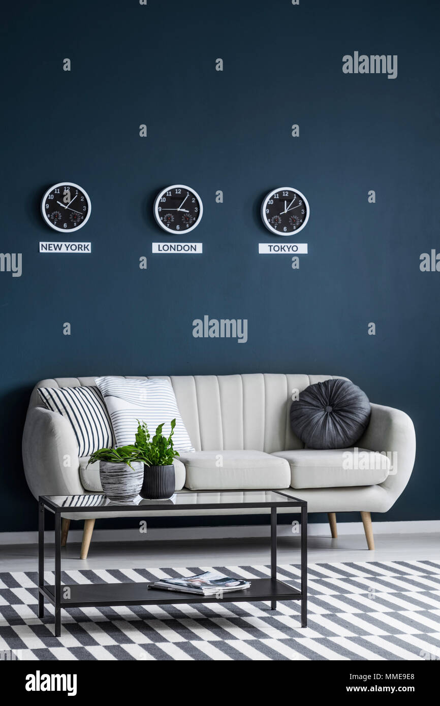 Uhren, die die Stunde in verschiedenen Zeitzonen auf einem dunklen blauen Wand, über eine komfortable beige Sofa in einem modernen Apartment Innenraum Stockfoto
