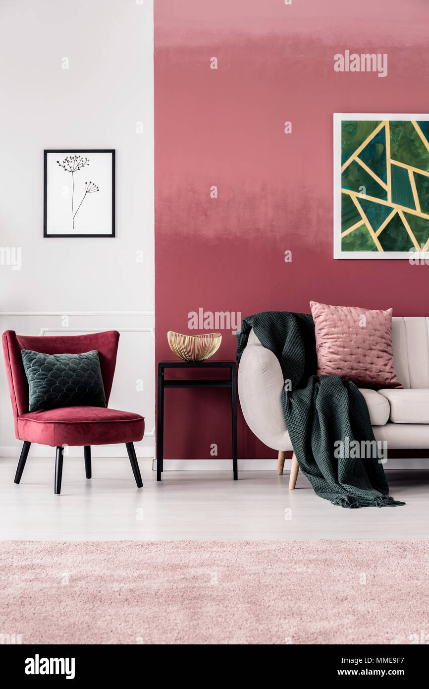 Feminine Wohnzimmer Einrichtung mit burgunderroten Sessel und Dunkelgrün Decke auf einem beigen Sofa gegen ein ombre Wand Stockfoto