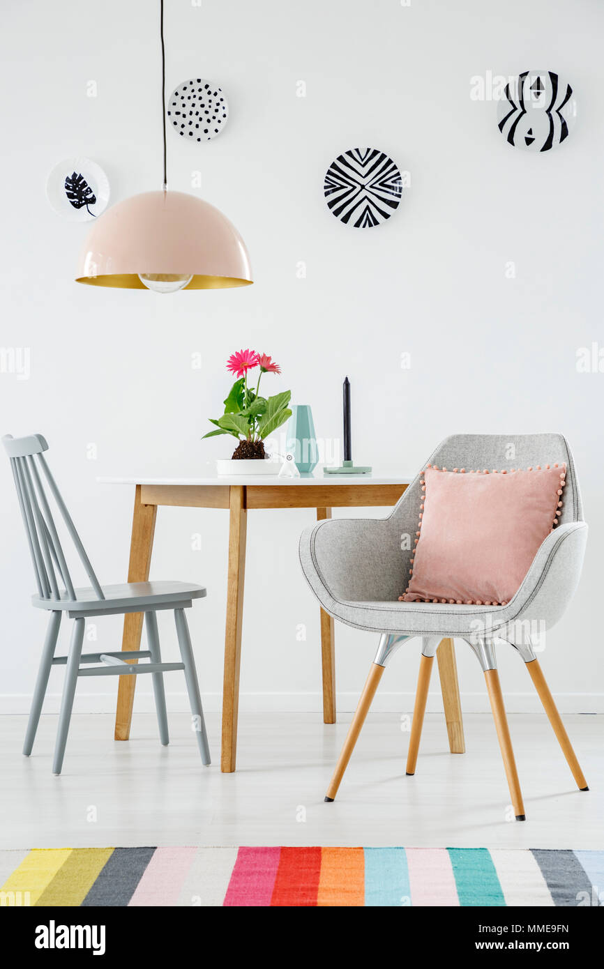 Vorderansicht eines Esstisch, Stuhl, retro Sessel mit einem Kissen, bunten Teppich, Lampe und Platten auf der weißen Wand Stockfoto
