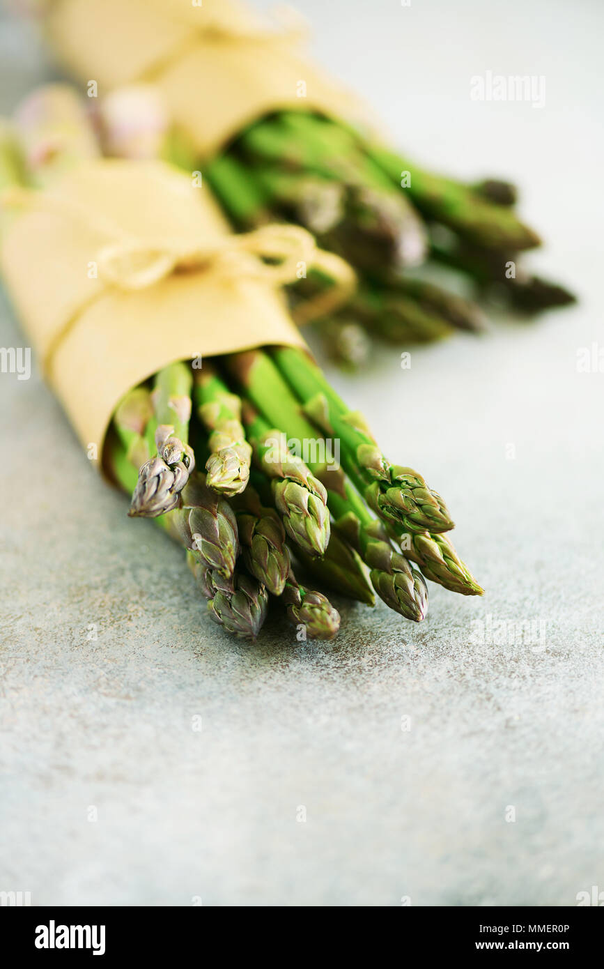 Bündel frischer Spargel auf Grau backgrouns. Spargel auf Handwerk Papier mit packthread. Raw, vegan, Vegetarisch und sauber essen Konzept Stockfoto