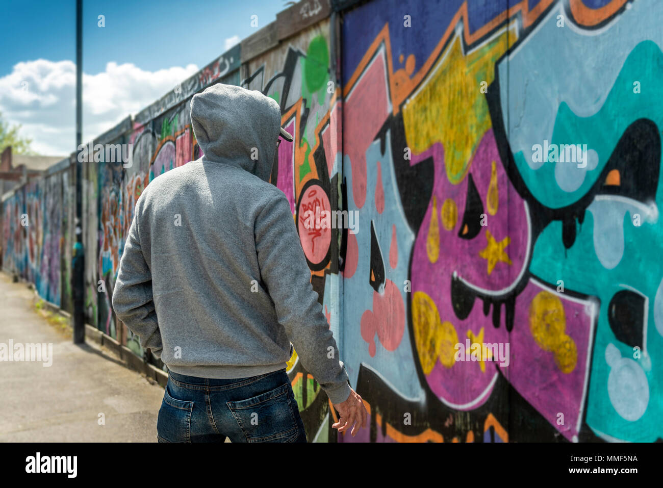 Rückansicht eines männlichen trägt ein Hoodie stehend durch eine Wand von Graffiti, Street Crime Konzept. Stockfoto