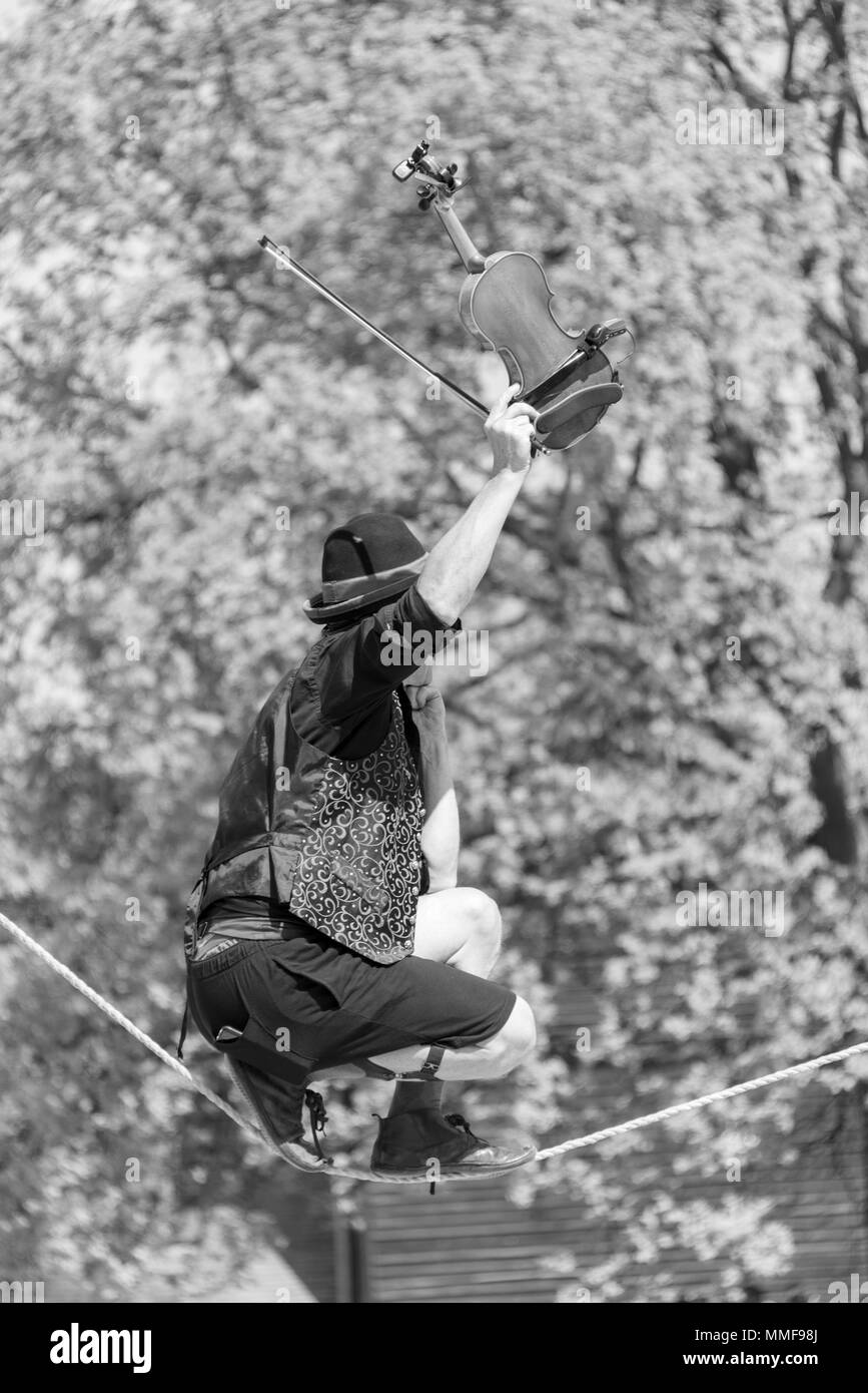 Schwarz-weiß Fotografie Street Performer walking Seil und spielen Violine Baum im Hintergrund Stockfoto