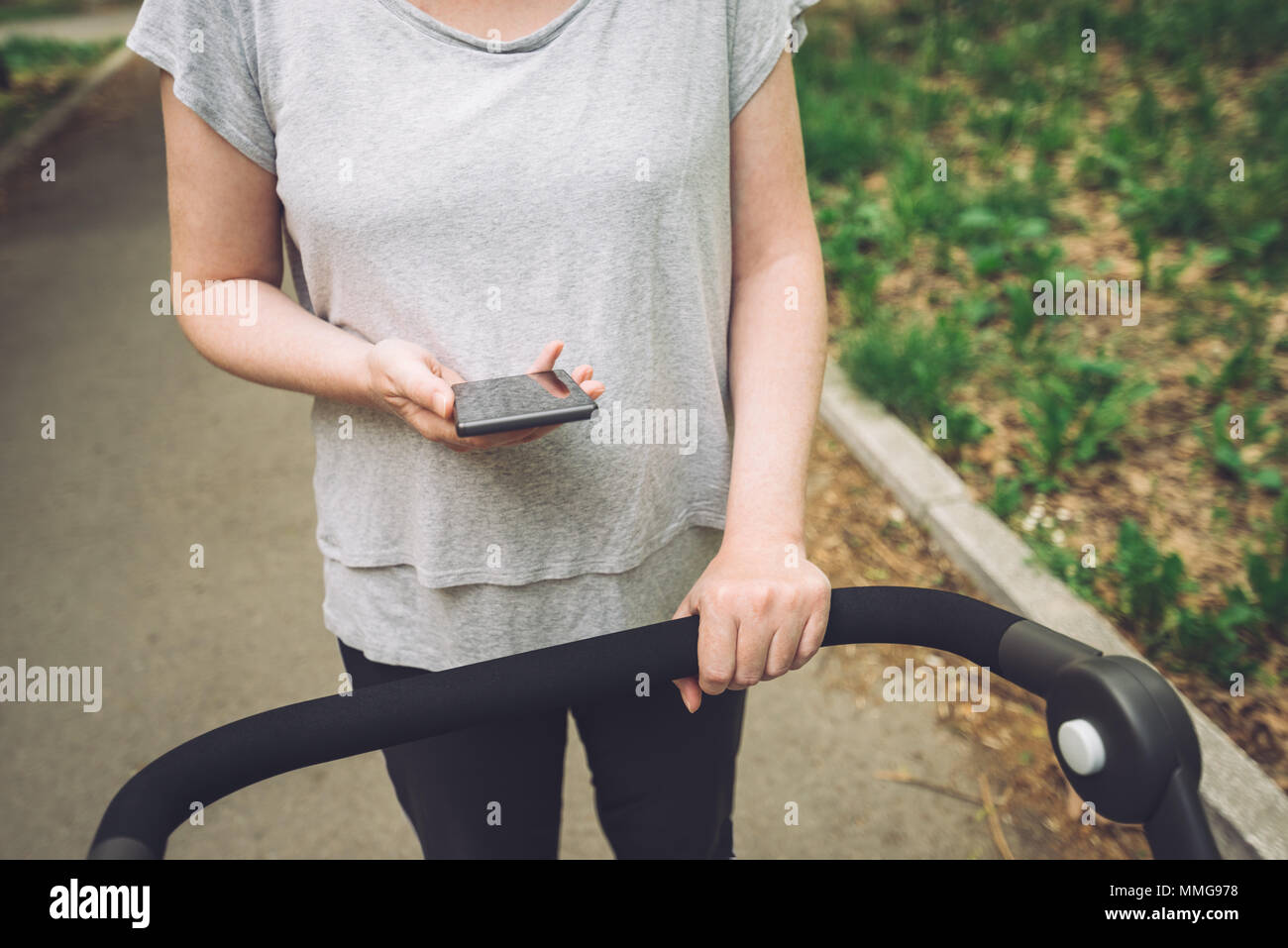 Mutter schieben Kinderwagen und Lesen von Sms auf Smart Phone beim Gehen auf der Straße im Casual Sport Kleidung Stockfoto