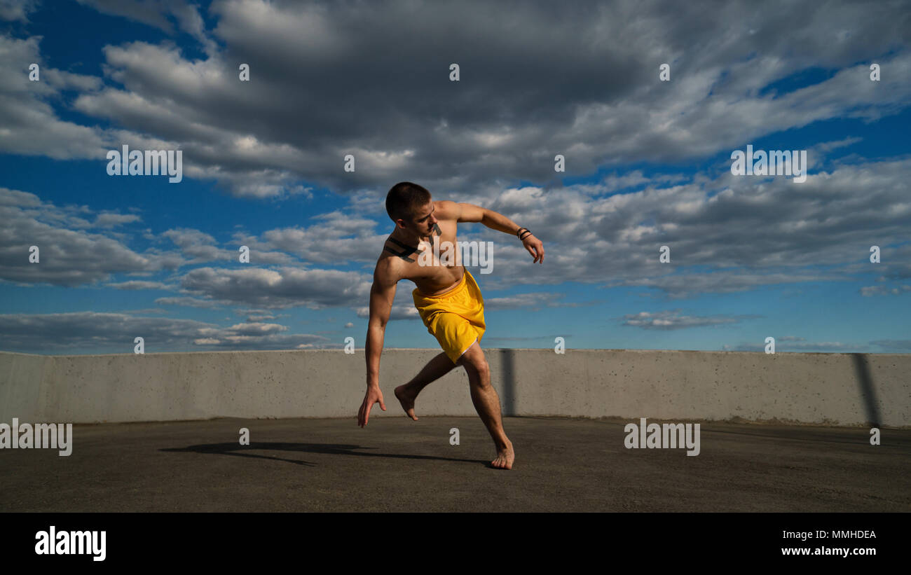 Austrickst, auf die Straße. Kampfsportarten Mann führt Sprung mit Unterstützung seiner Hand barfuß. Bhudda Verkürzungen von unten gegen den Himmel. Stockfoto