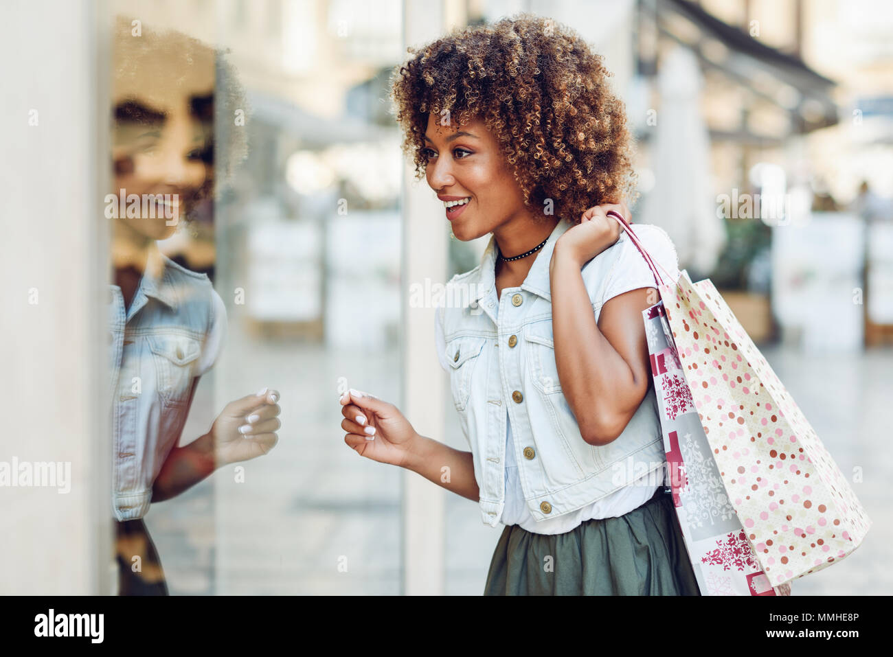 Junge schwarze Frau vor einem Schaufenster in einer Einkaufsstraße. Afrikanisches Mädchen mit Afro Frisur legere Kleidung. Stockfoto