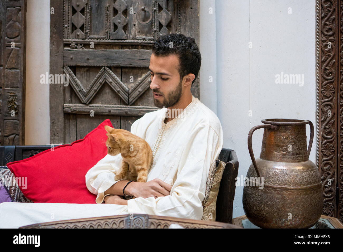 Junge muslimische Mann hält eine gelbe Katze vor einem geschmückten Wand Stockfoto