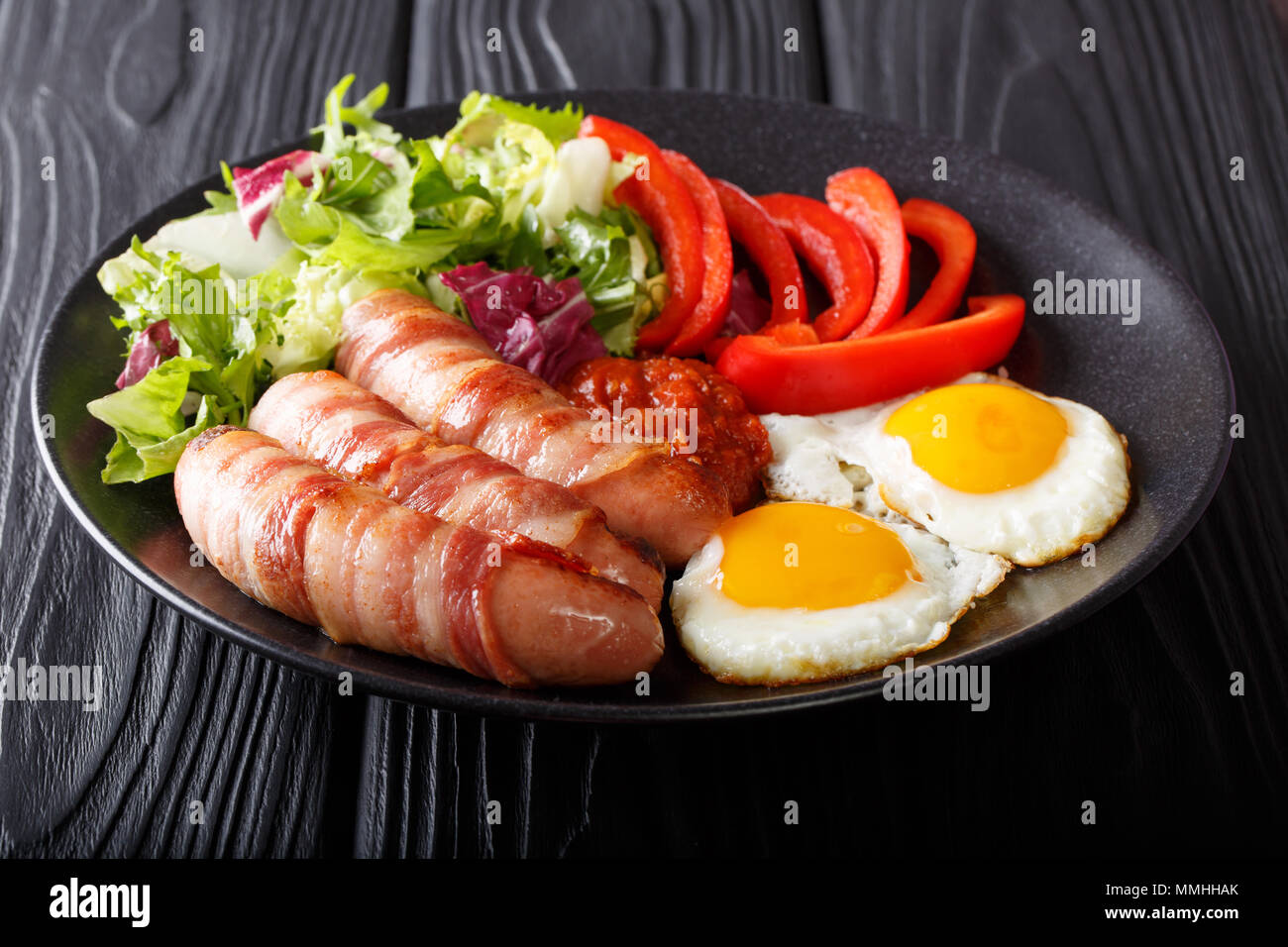 Englisches Frühstück: Schweine in Decken gebratene Würstchen, Speck, Eier, Soße und Salat in der Nähe verpackt - bis auf einen Teller auf dem Tisch. Horizontale Stockfoto