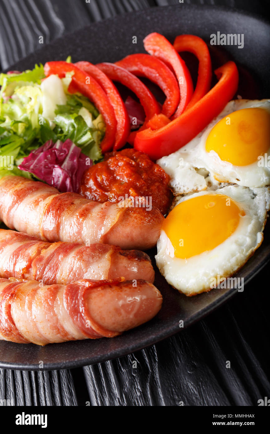 Gebratene Würstchen eingewickelt in Speck, Eiern und frischem Salat close-up auf einem Teller. Vertikale Stockfoto