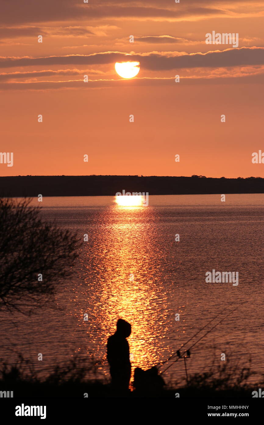 Silhouette von Lone fischer See bei Sonnenuntergang, die Casting ist eine Reflexion über das Wasser mit dem Hintergrund, die die Mauren Stockfoto