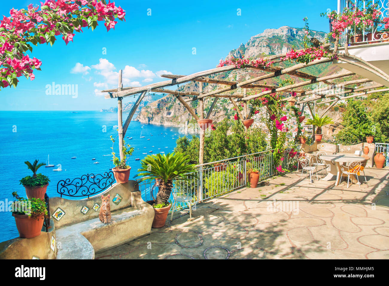 Schöne Terrasse mit Tisch, Stühlen und blühenden Blumen und mit Blick auf das Meer und die Berge in der Nähe von Positano, Amalfiküste, Italien Stockfoto