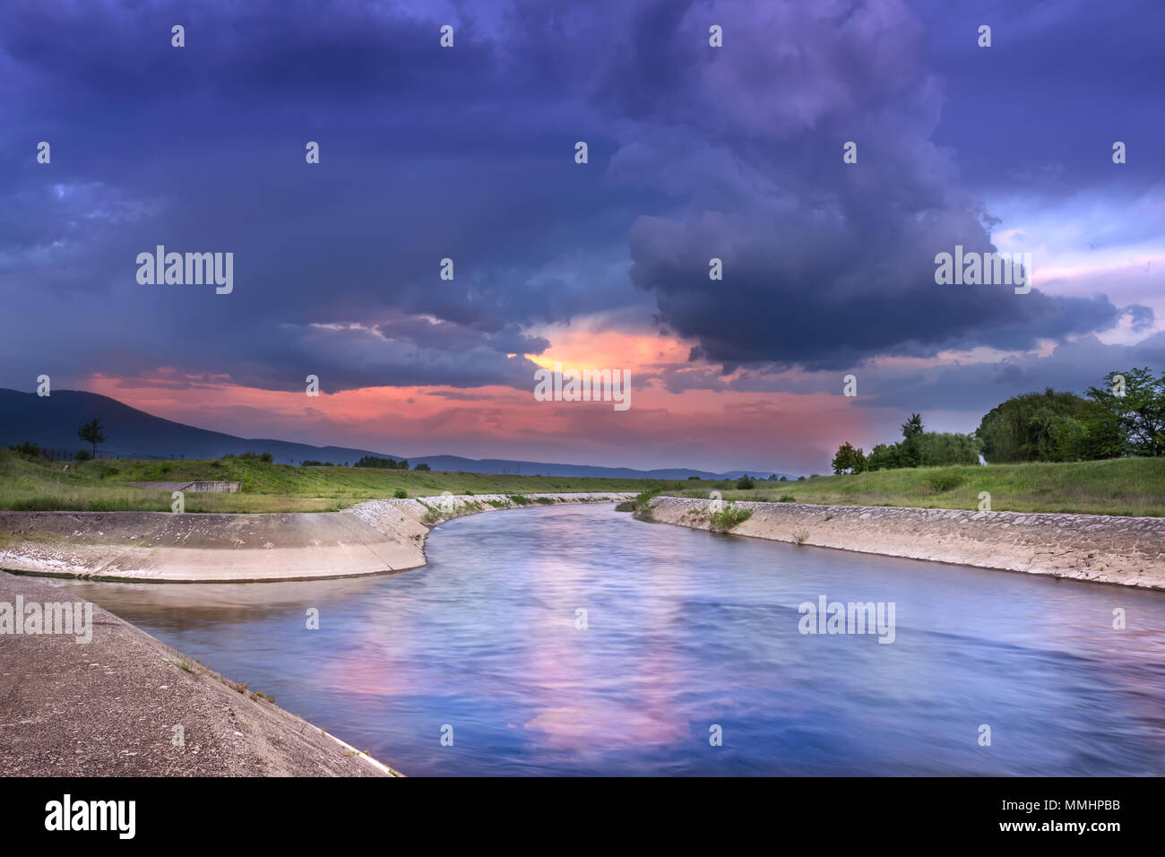 Erstaunlich, dramatischer Sonnenuntergang Farben und flauschige Wolken über reflektierende, kurvenreichen Fluss blaue Stunde Zusammensetzung Stockfoto