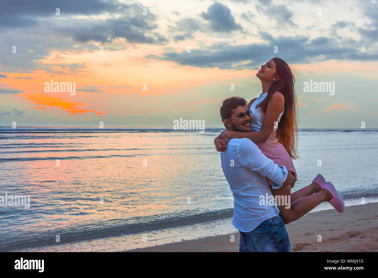 Mann hob seine Freundin am Strand im Sonnenuntergang Stockfoto