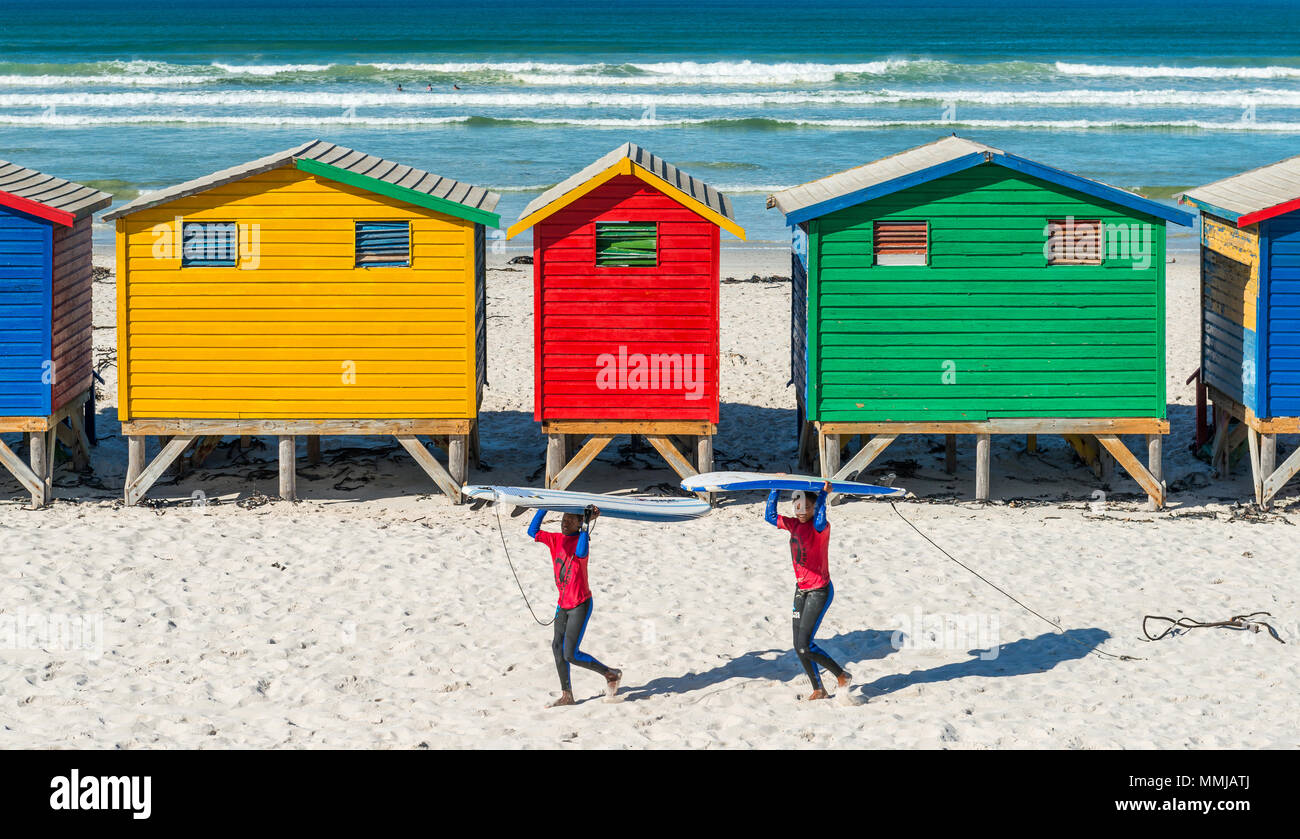 Lächelnden jungen Südafrikanischen Surfer ihre surfbretter am Strand von Muizenberg, berühmt für die bunten Badekabinen, Südafrika. Stockfoto