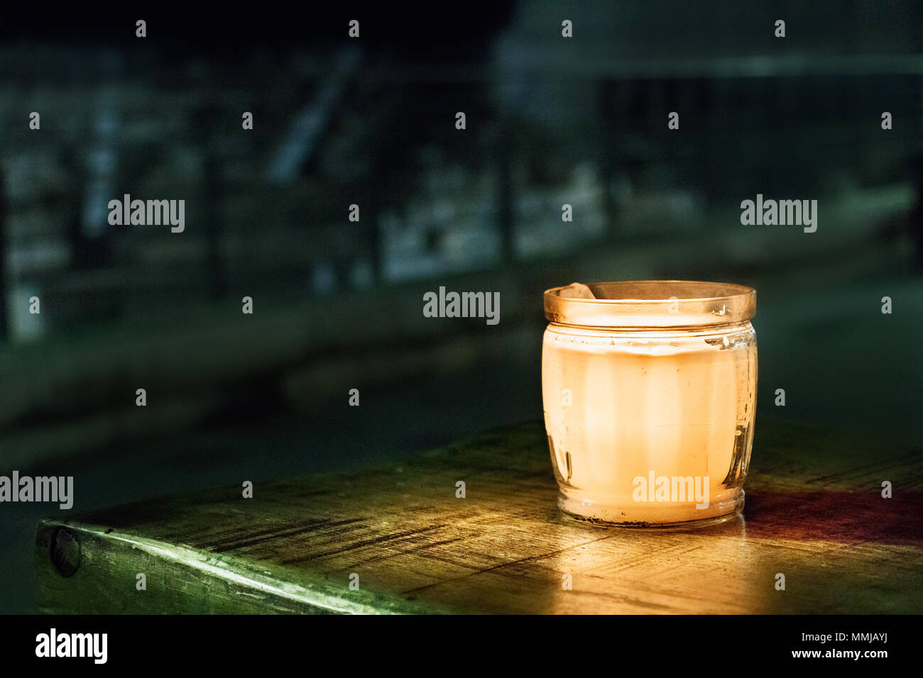 Eine Kerze auf einem Glas, auf einem Holztisch, im Freien, mit dem antiken griechischen Theater als Hintergrund in Patras, Griechenland. Stockfoto