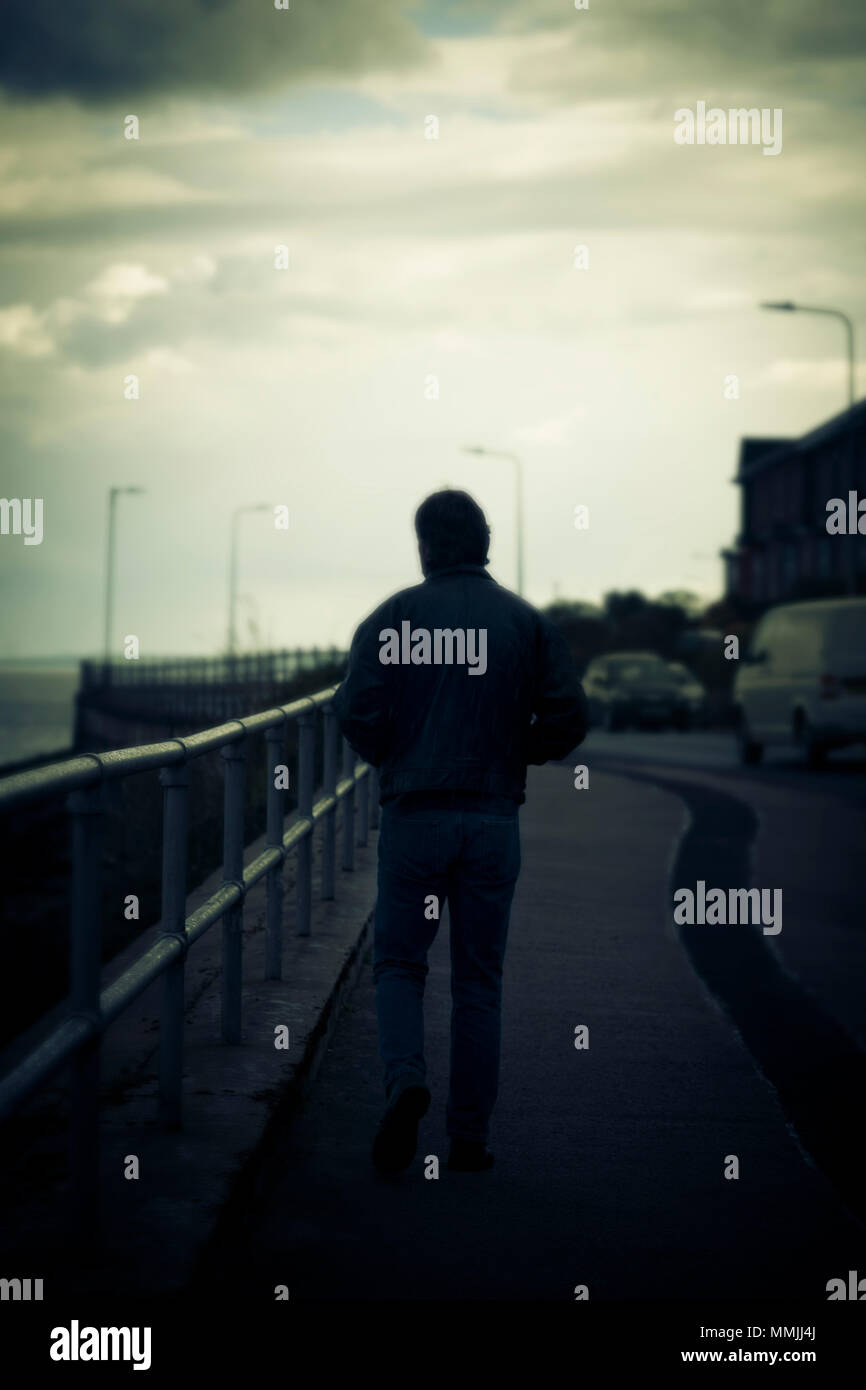 Silhouette von Mann zu Fuß auf dem Weg neben dem Meer, mit der Straße auf der rechten Seite Stockfoto