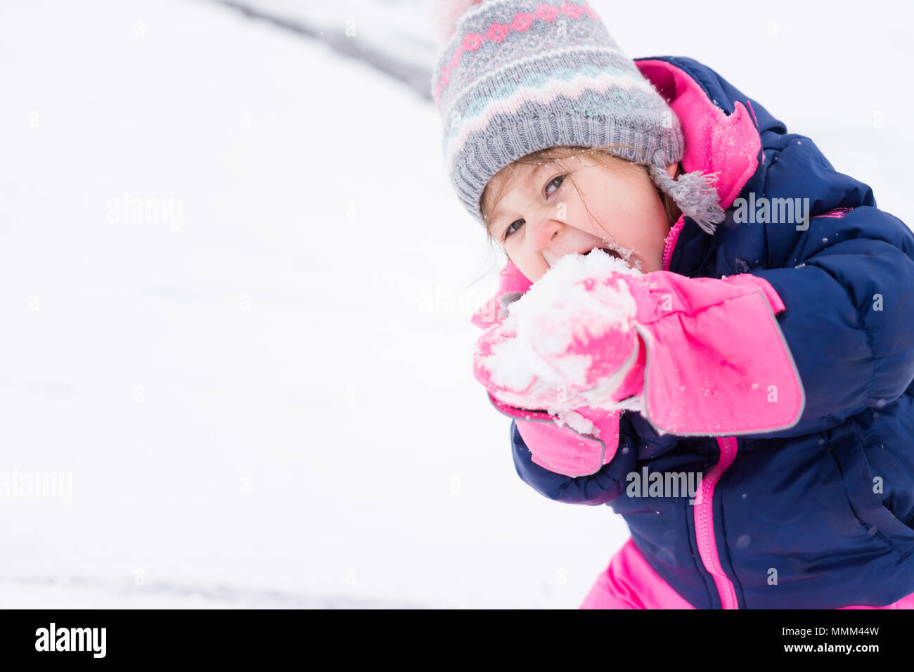 Kleine Mädchen in rosa und blau glücklich essen Schnee gebündelt Stockfoto