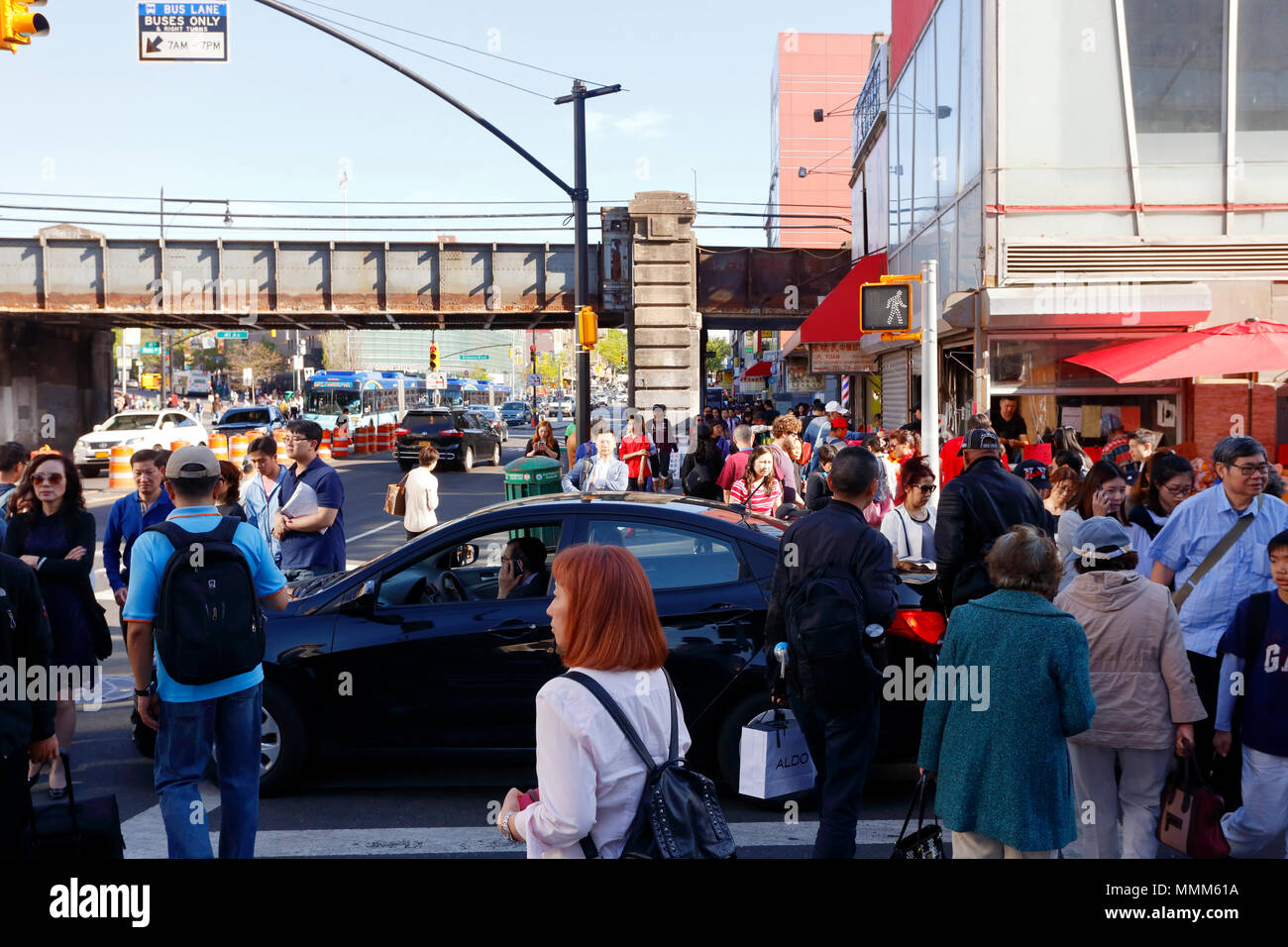Ein Fahrer sitzt bei einem Handyanruf an einem Straßenübergang, während Fußgänger um das Fahrzeug in Downtown Flushing, New York, NY, 法拉盛華埠, 法拉盛 華裔美國人, 紐約 Stockfoto