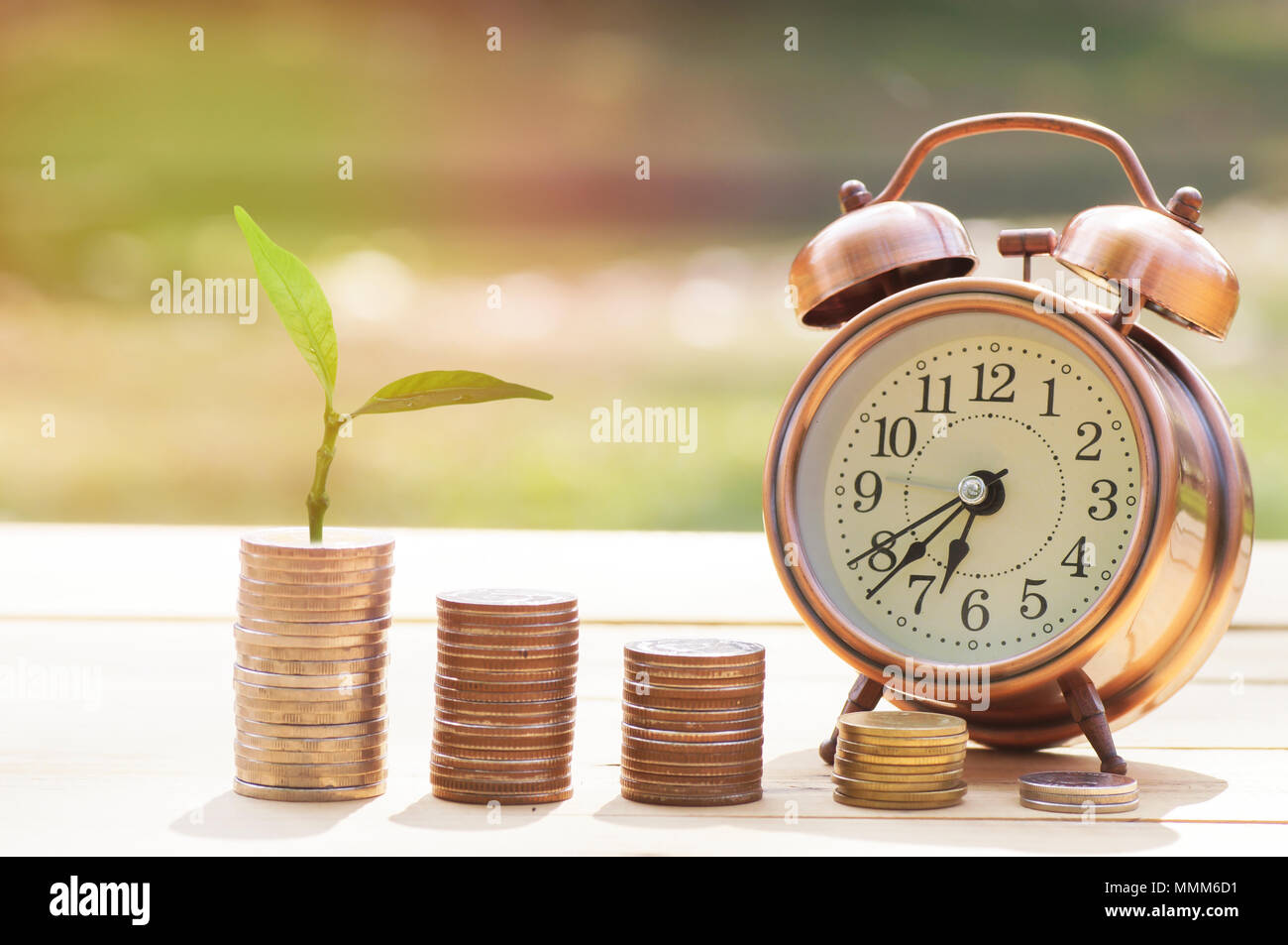 Stapel von Münzen und kleinen Baum mit Alarm clcok auf Holz Tisch, Konzept in Wachsen und sparen Sie Geld Stockfoto