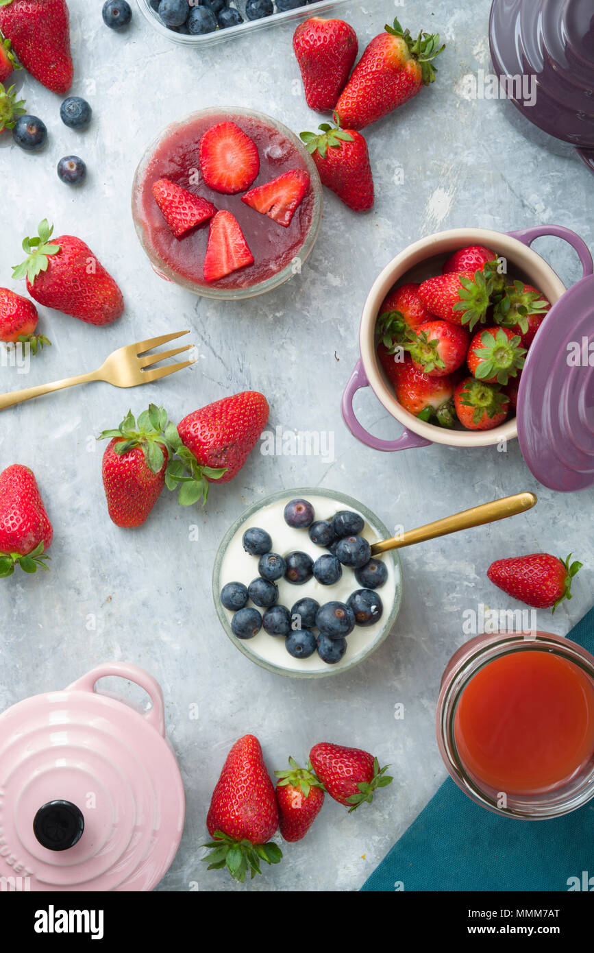 Blick von oben auf die Erdbeeren und Blaubeeren edle Käsekuchen in Glas Glas über einen grauen Hintergrund, mit farbigen Cocotte in Blaubeeren, strawberri Stockfoto