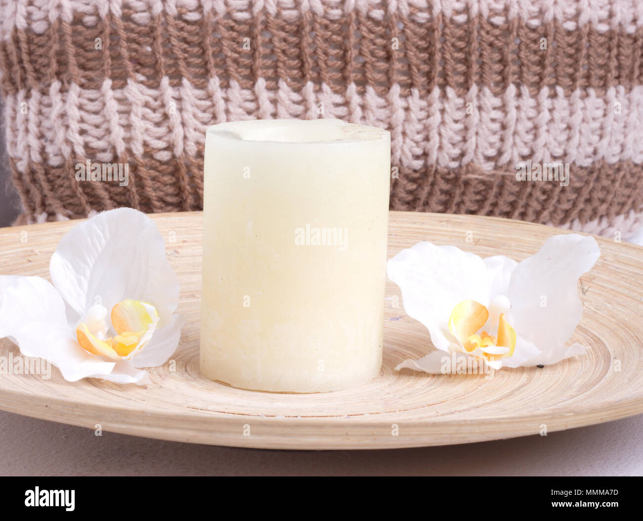 Weiße Kerze mit Blumen in der Nähe ein gestricktes Polster Stockfoto