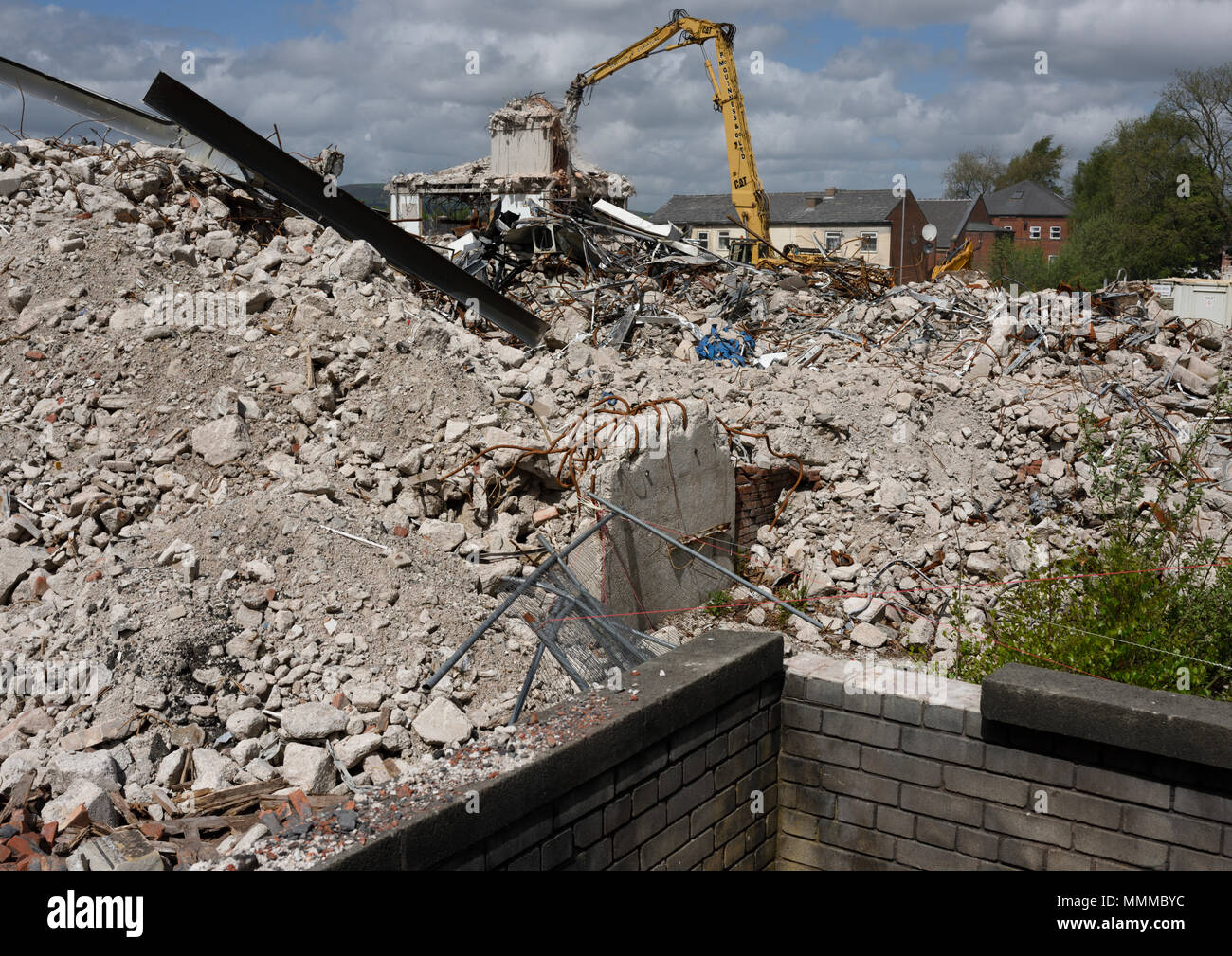 Betonschutt und Abfall auf und Ziegelwand beim Abriss Baustelle mit Abbruchbagger im Hintergrund in Bury lancashire vereinigtes Königreich Stockfoto