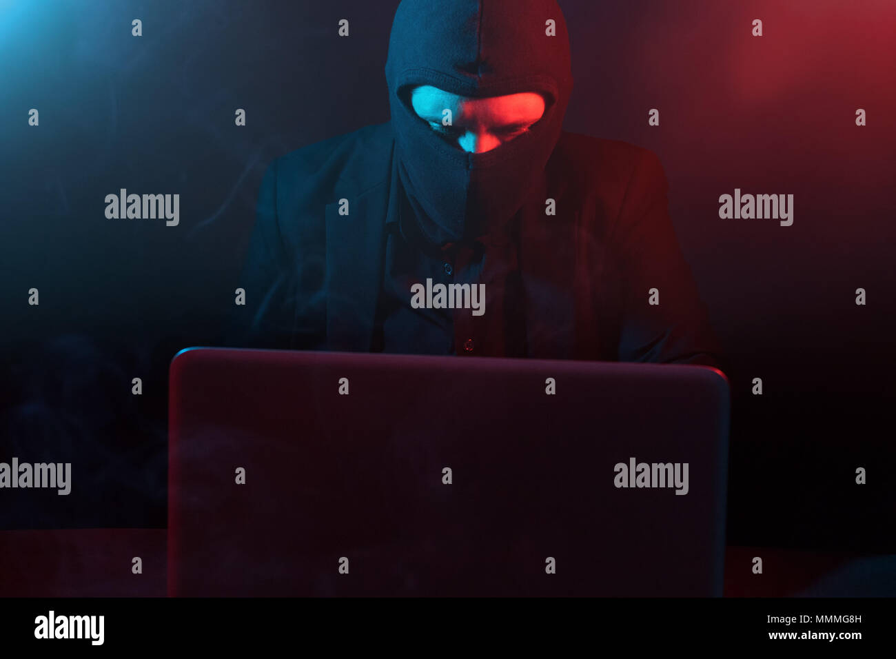 Wütend Computerhacker in Anzug stehlen Daten vom Laptop durch rote und blaue Licht beleuchtet Stockfoto