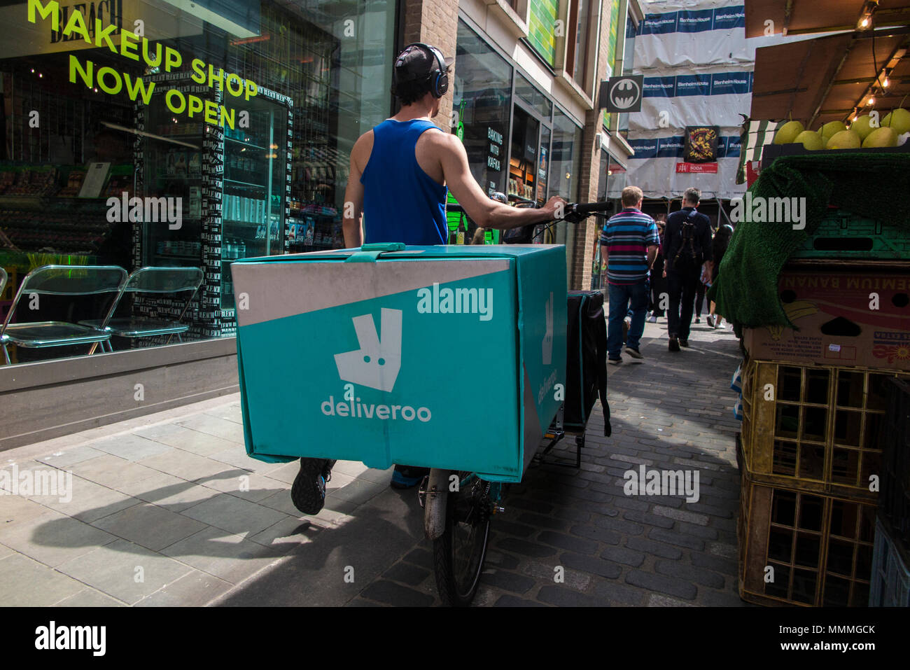 Eine Deliveroo rider Kopfhörer tragen schiebt sein Fahrrad durch einen gedrängten Markt Stockfoto