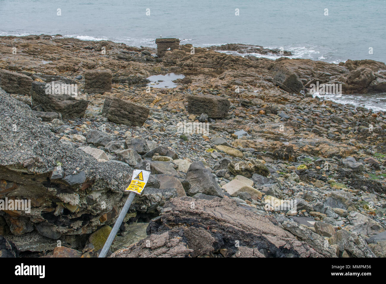 Gefahr lose Felsen Zeichen, verbogen worden ist und ein Umkippen vor einige lose Felsen an der Küste in Newlyn in Cornwall. Stockfoto