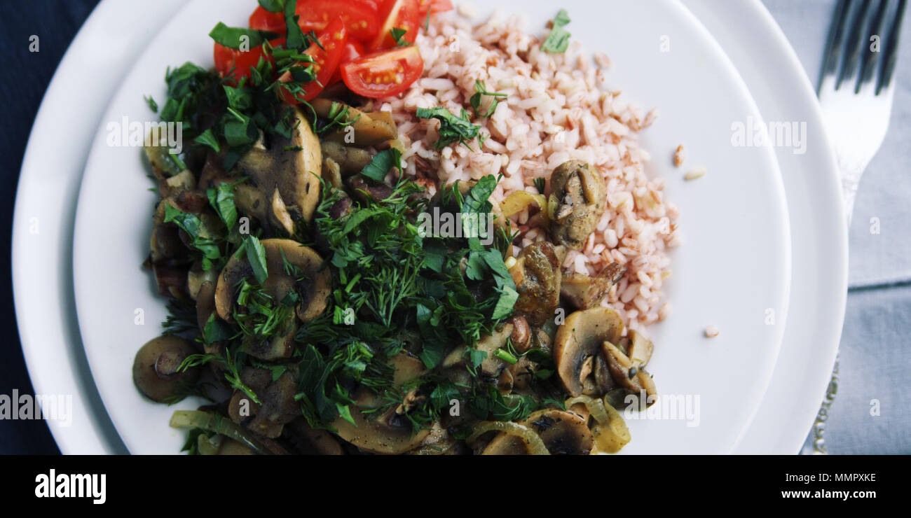 Roter Reis mit Pilzen und Tomaten. Vegane Gerichte. Europäische Küche. Einfach gesundes Mittagessen. Vegetarisches Reisgericht auf dem weißen Teller. Close Up. Wi Stockfoto