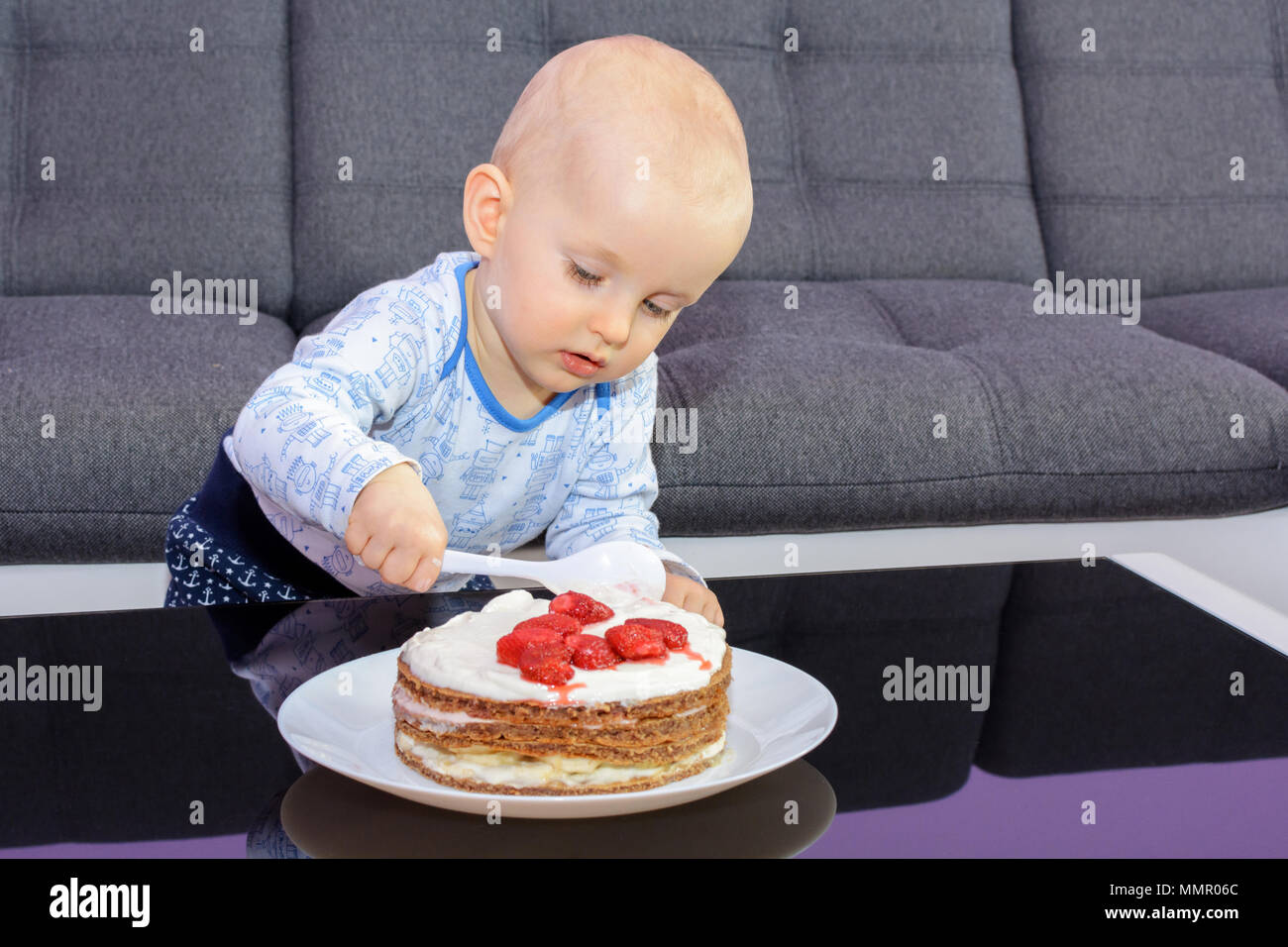 Der erste Geburtstag Feier eines kleinen Jungen. Little Boy essen Geburtstag Kuchen mit einem Löffel, alles Gute zum Geburtstag. Kleinkind am Tisch mit Kuchen. Stockfoto