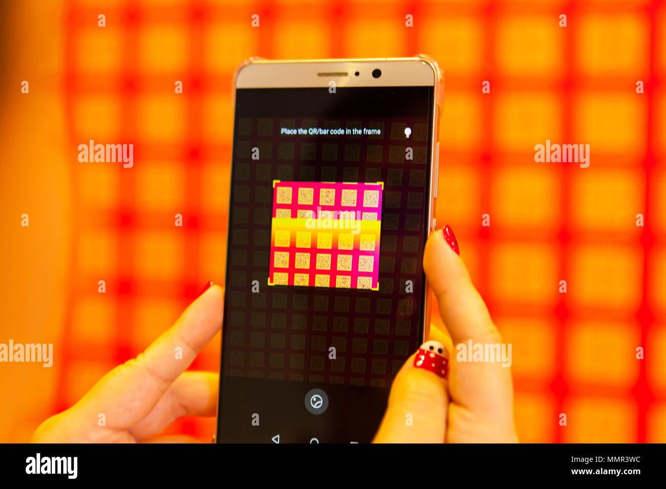 Eine Dame Hand hält ein Handy Smartphone zu scannen QR-Code an der Wand Stockfoto