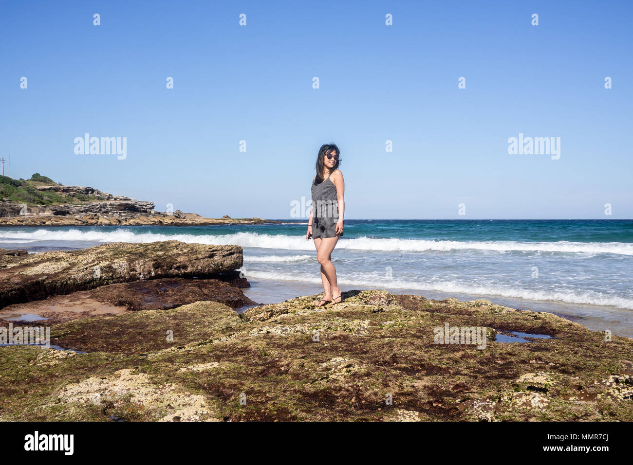 Junge Frau mit Sonnenbrille auf dem felsigen Ufer des Maroubra Beach, Sydney, Australien. Stockfoto