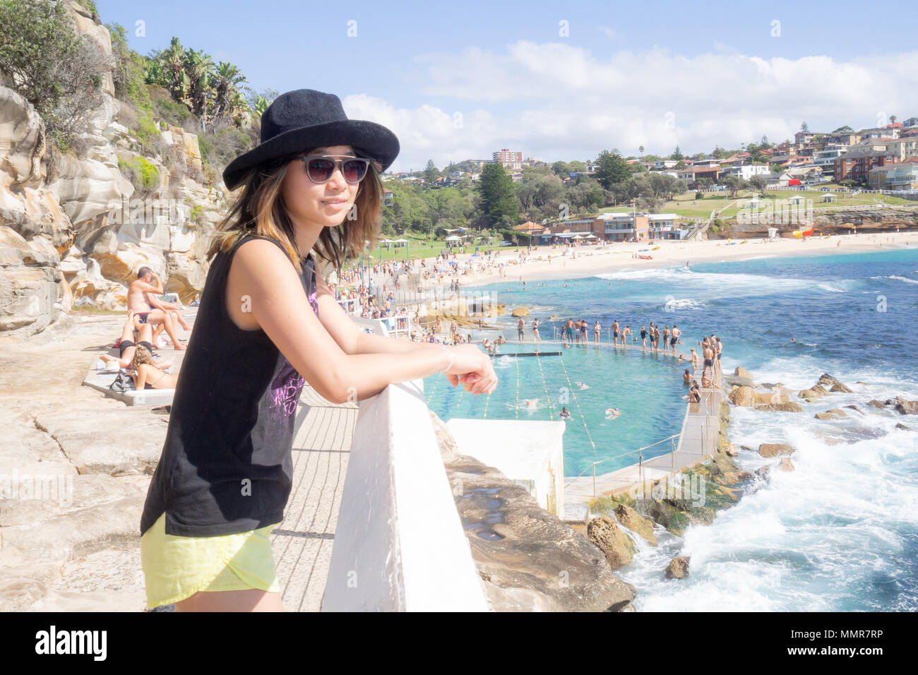 Junge Frau mit Hut und Sonnenbrille zu Fuß durch das öffentliche Schwimmbad in Bronte Beach in Sydney, Australien Stockfoto