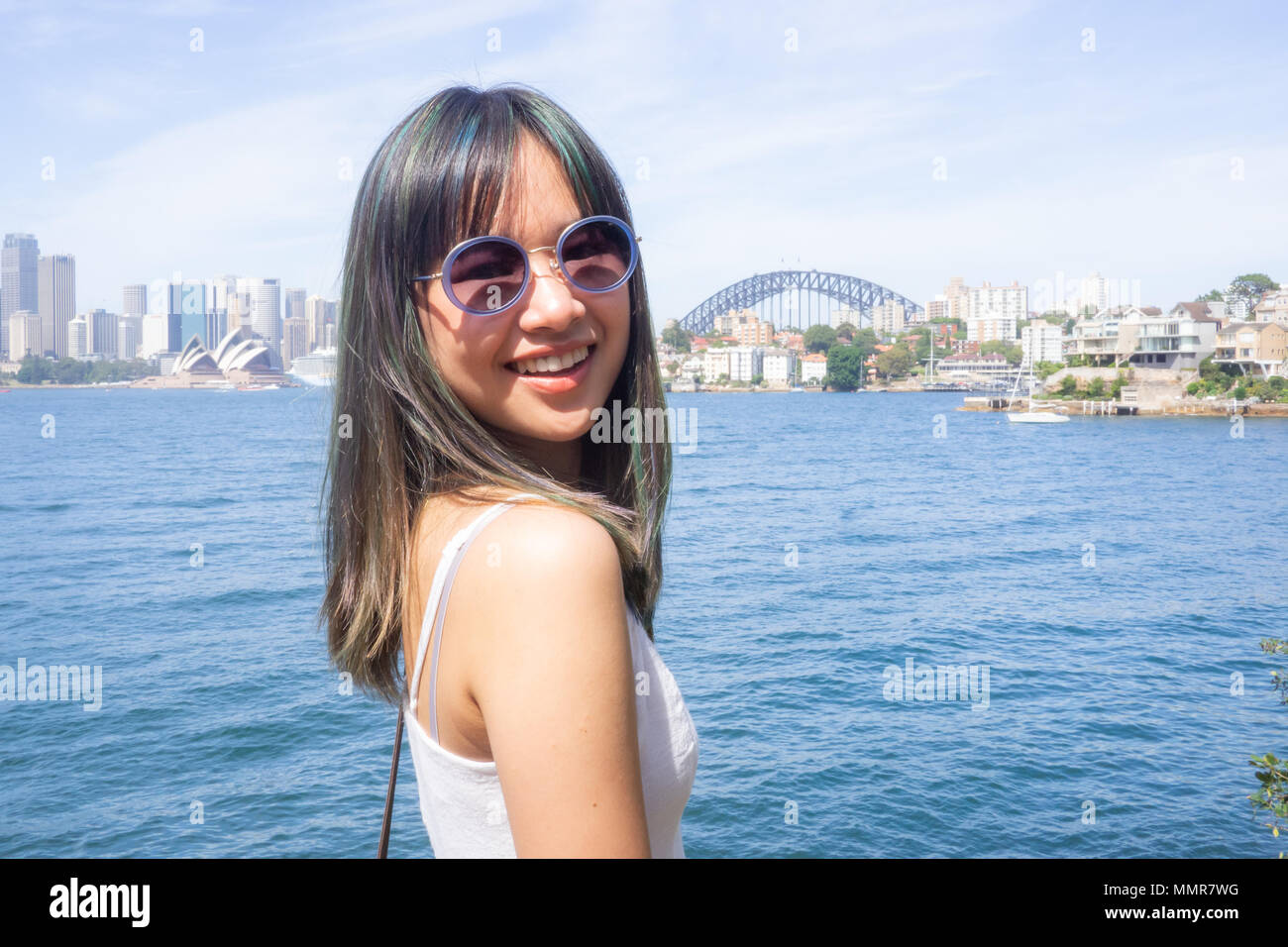 Junge Frau steht auf dem Hintergrund der schönen Sydney Skyline an einem sonnigen Tag in einem weißen Kleid und Sonnenbrille Stockfoto