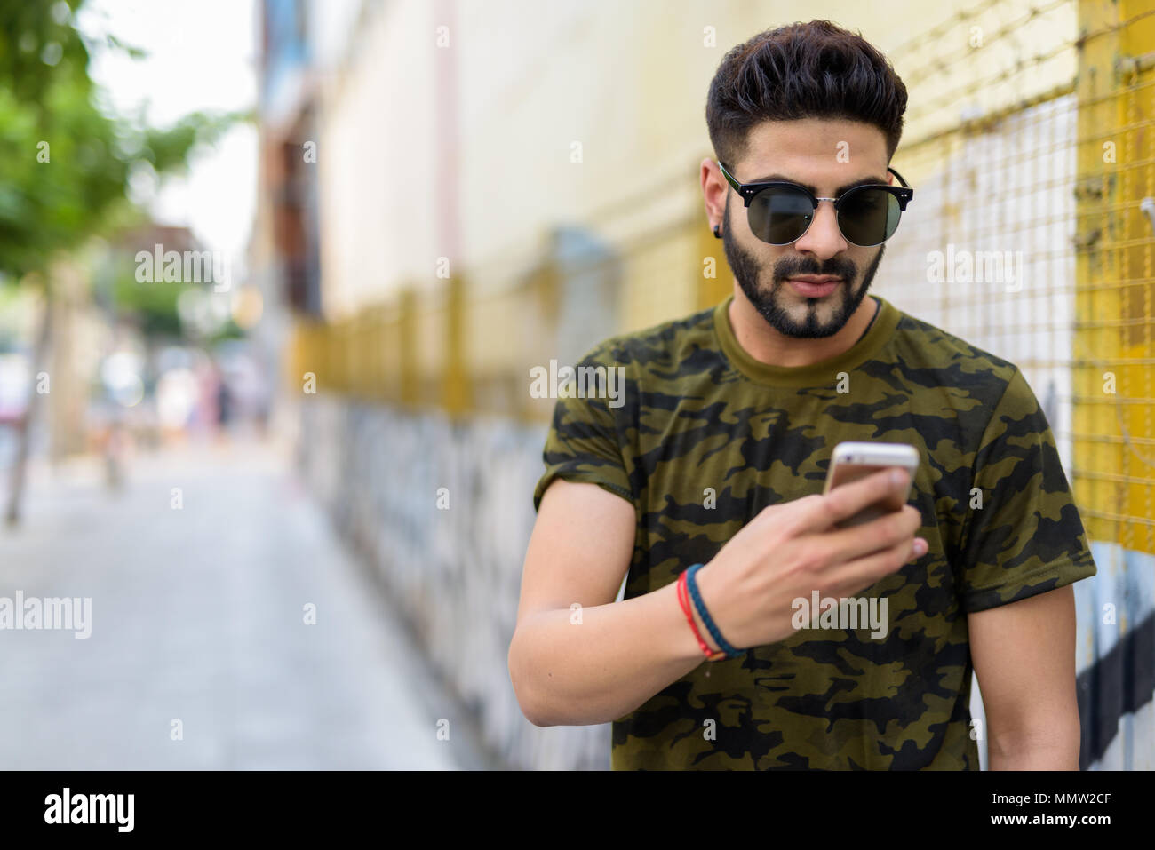 Junge schöne Indische mann Sonnenbrille tragen bei der Verwendung von Mobile Stockfoto