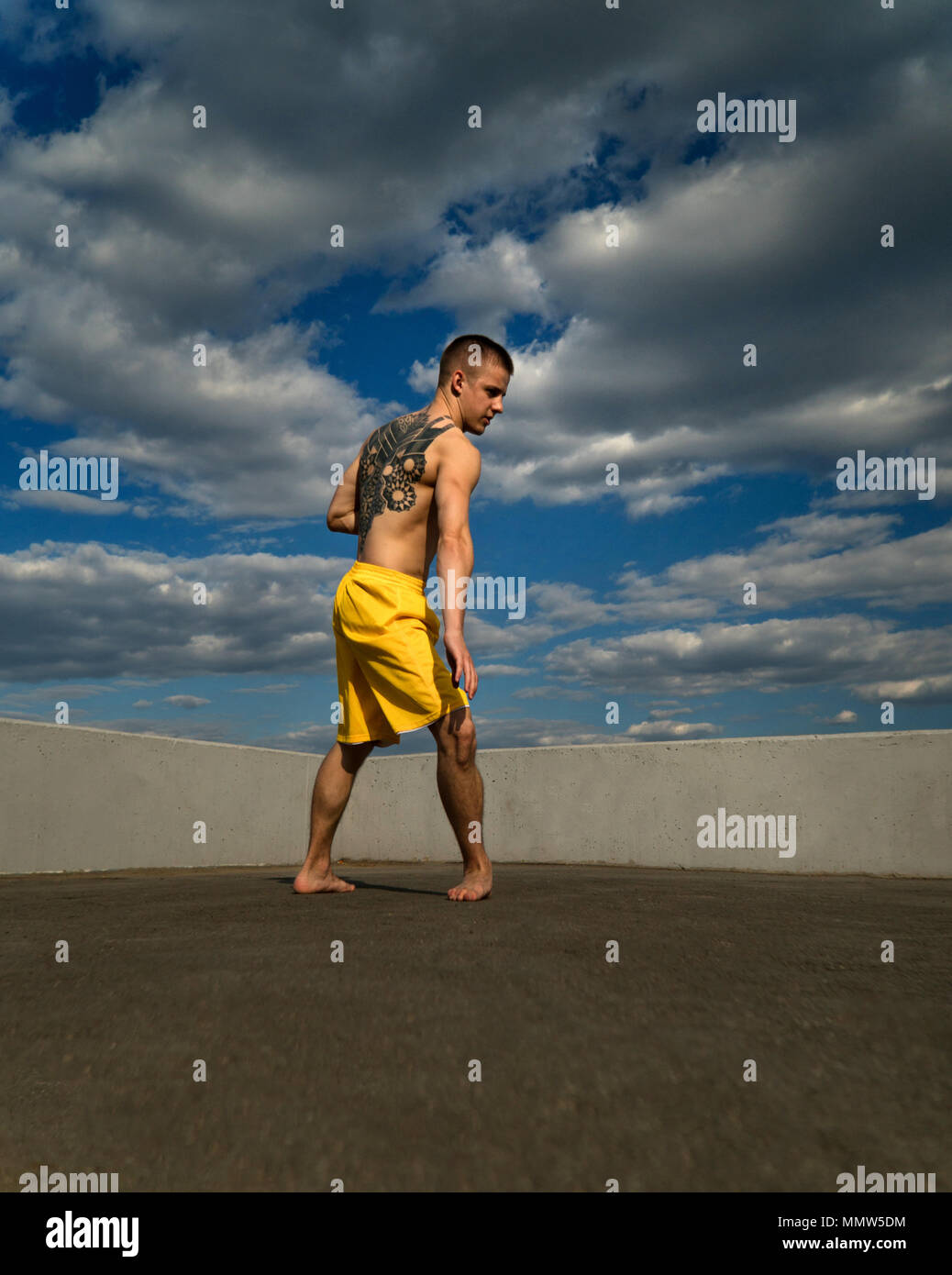 Austrickst, auf die Straße. Kampfsportarten Mann steht in Rack für Roundhouse Kick barfuß. Bhudda Verkürzungen von unten gegen den Himmel. Stockfoto