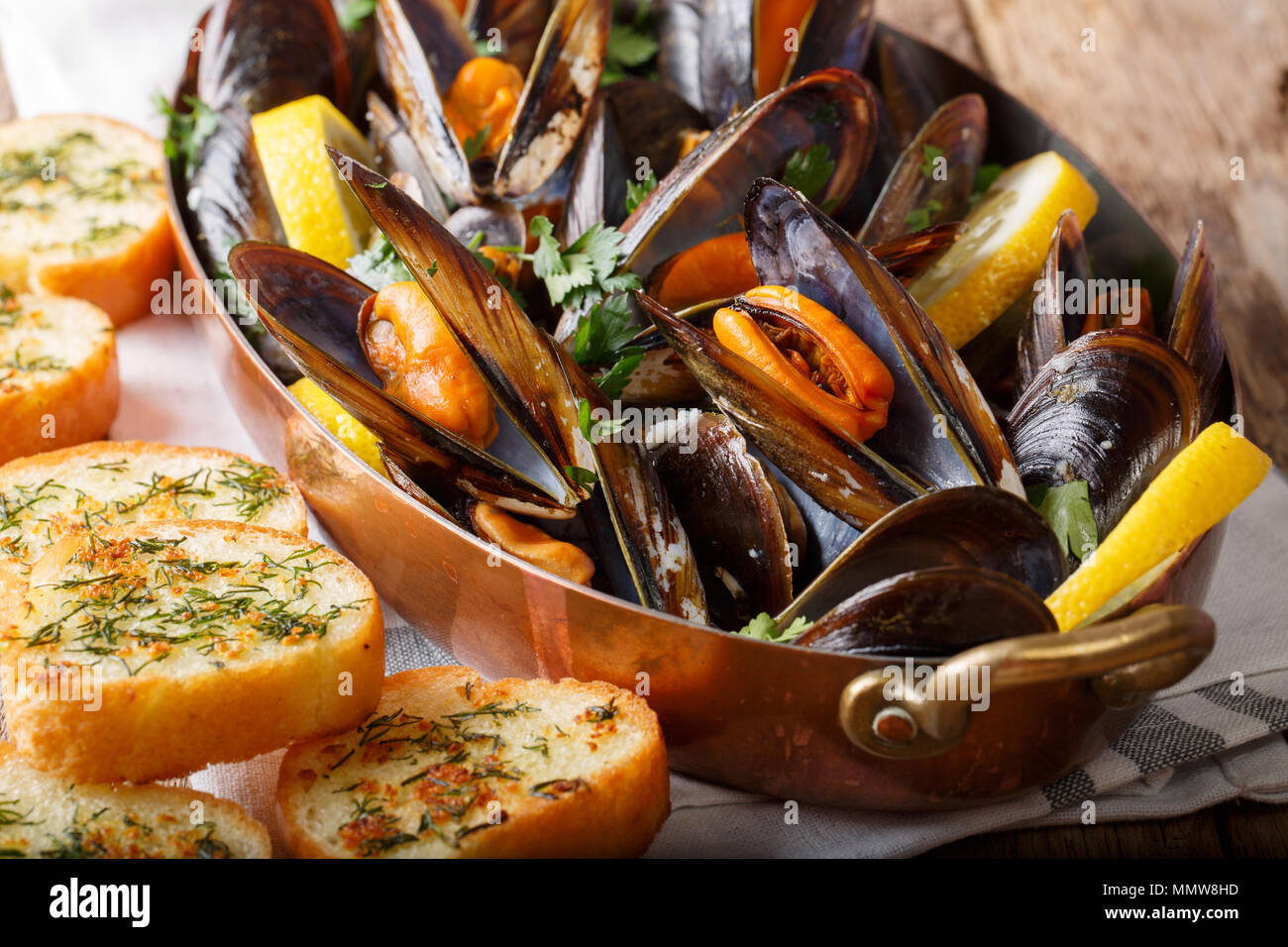 Französische Miesmuscheln mit Zitrone, Petersilie und Knoblauch close-up, das in einem Kupfertopf und Toast auf dem Tisch. Horizontale Stockfoto