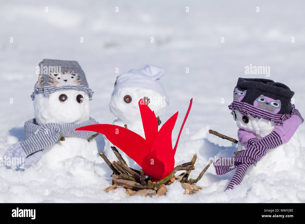 Süße kleine Schneemänner gekleidet für den Winter, drängten sich rund um ein Lagerfeuer versuchen, warm zu halten. Verschneite Szene in Norfolk, Großbritannien. Schneemann Tragen von Kleidung. Stockfoto