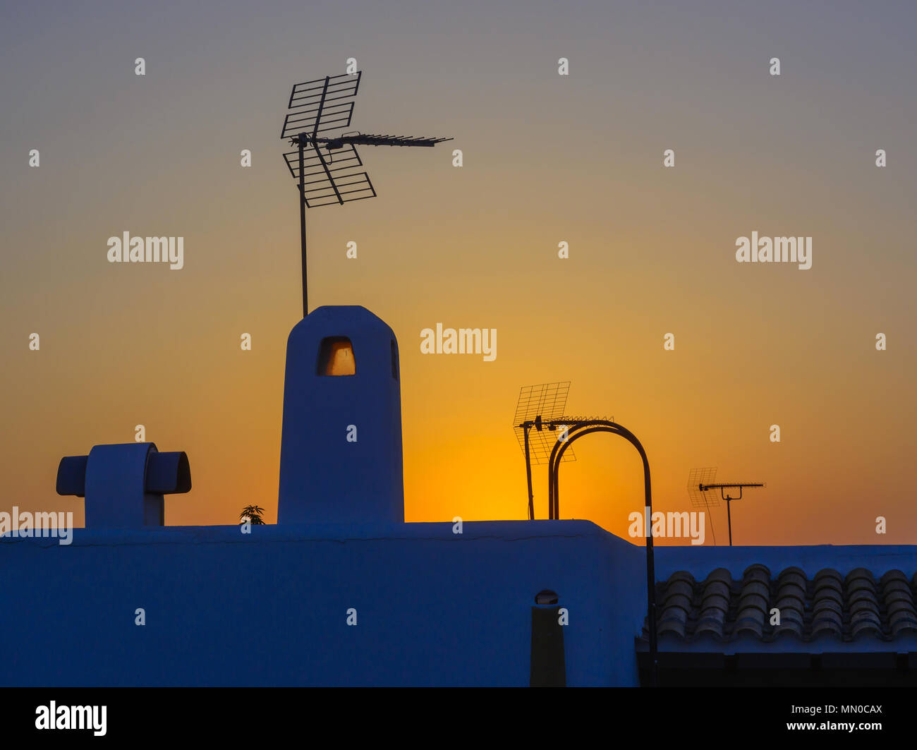 Analoge Antenne Silhouette am Dach bei Sonnenuntergang in gesättigtem Gelb, Rot und Blau Stockfoto