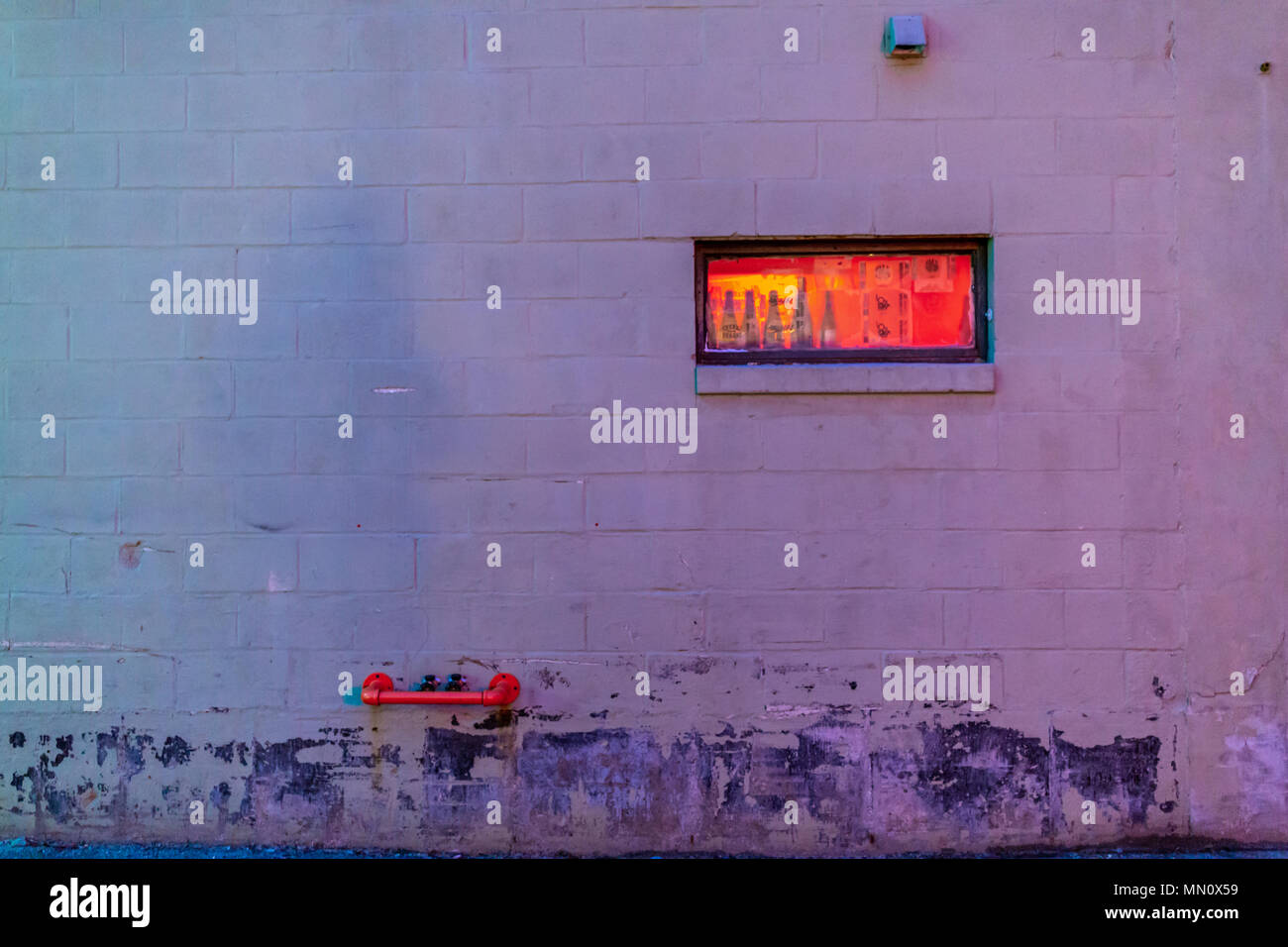 Bild in der Nacht von einem kleinen rechteckigen Fenster, orange leuchtende in einem konkreten Block Wand in Portland Maine Stockfoto