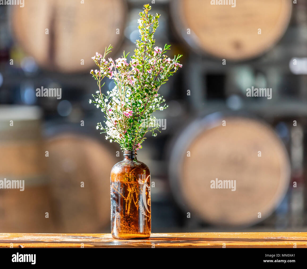 Frisches Wild wachsende Blumen in einer braunen Flasche mit grossen Fässer im Hintergrund Stockfoto